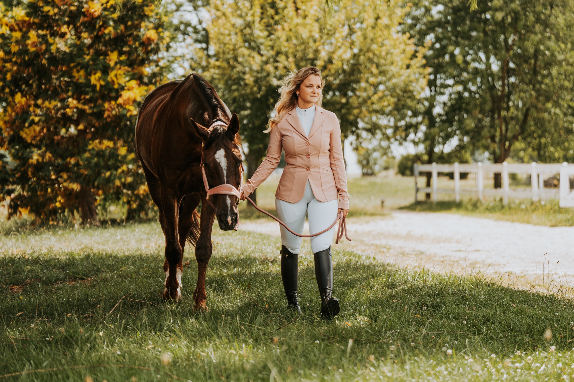 Žena vede hnědého koně po trávě v areálu